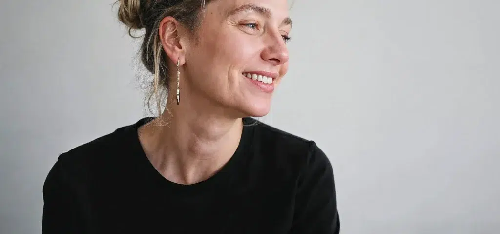 Woman with blonde hair smiling warmly in a minimalist portrait